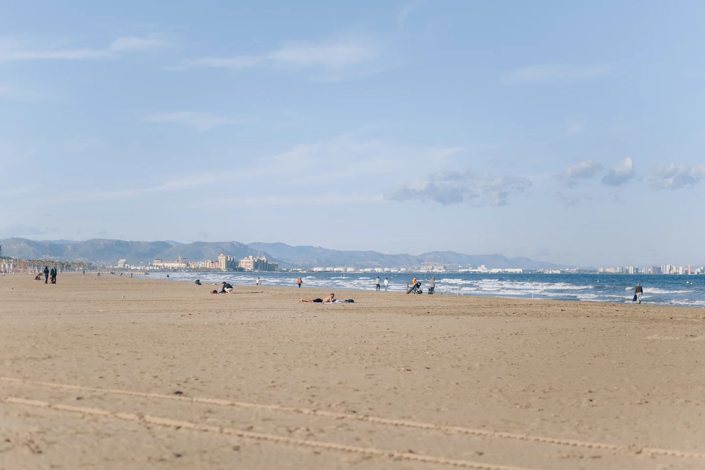 Playa de arena con personas junto a la orilla y montañas al fondo
