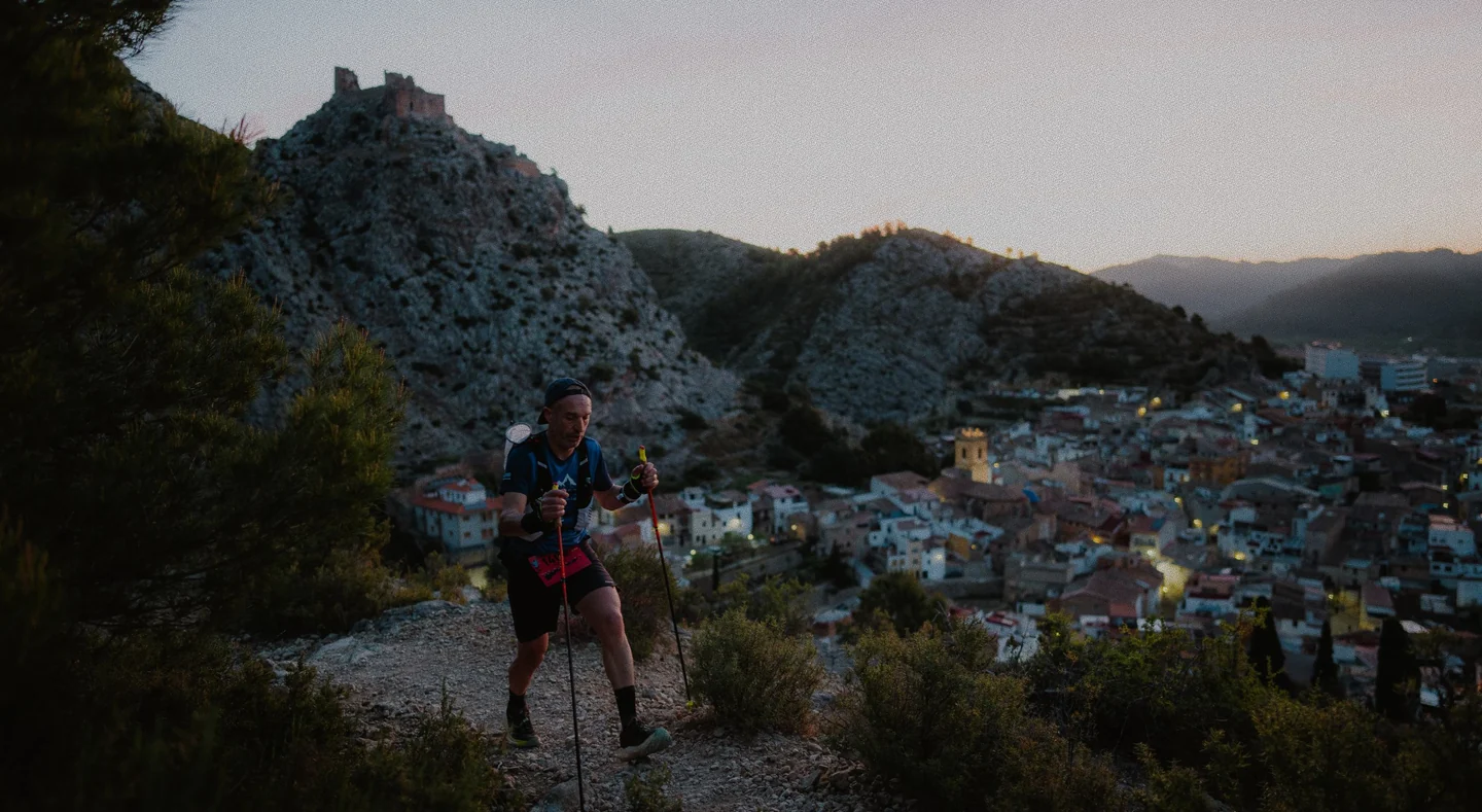 Corredor con bastones en un sendero sobre un pueblo entre montañas